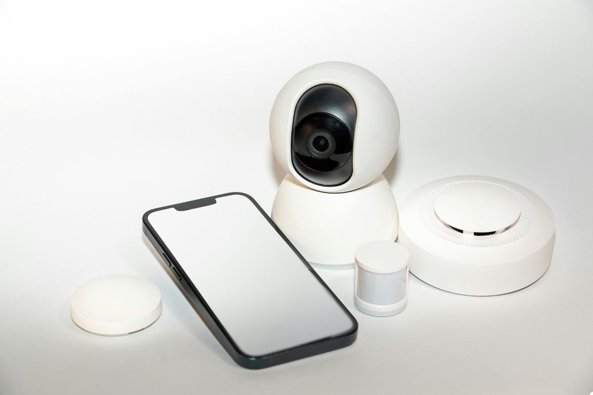 Smart home security camera, smartphone, and smoke alarm arranged on a clean white background for home safety solutions. 