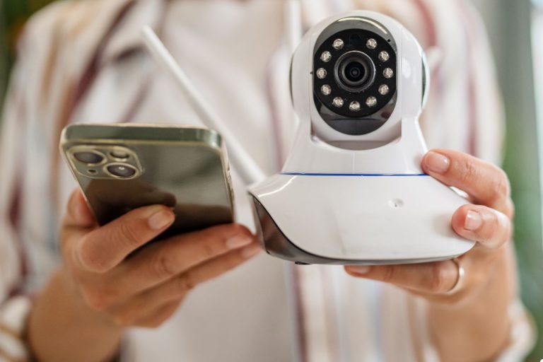A woman holds a smartphone while observing a security camera, showcasing a blend of technology and surveillance.
